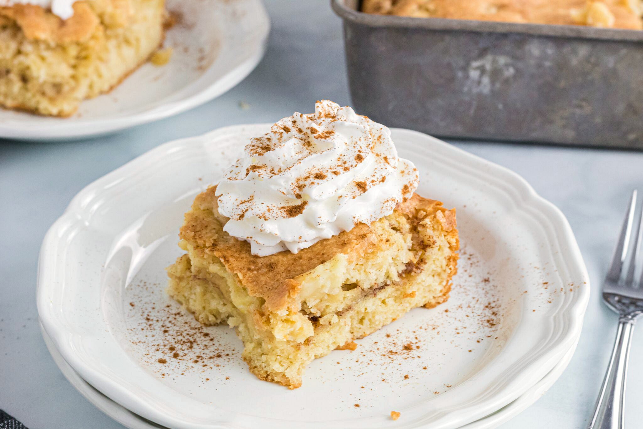 A piece of cake with apples in the middle and whipped cream and cinnamon sprinkled on top 