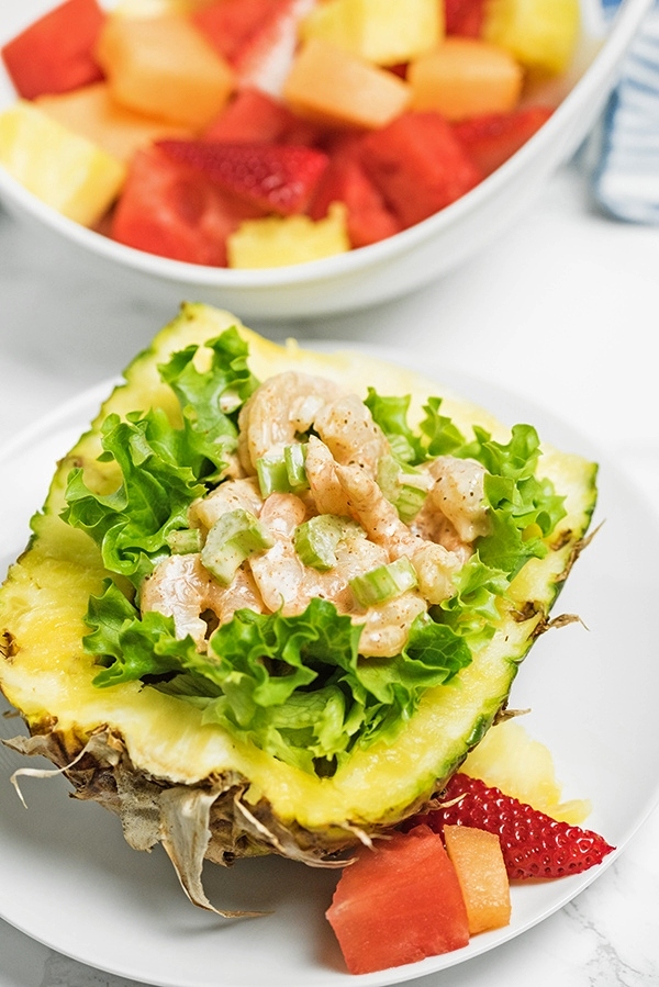 Delicious shrimp salad on a bed of lettuce inside a halved pineapple surrounded by fruit is amazing!
