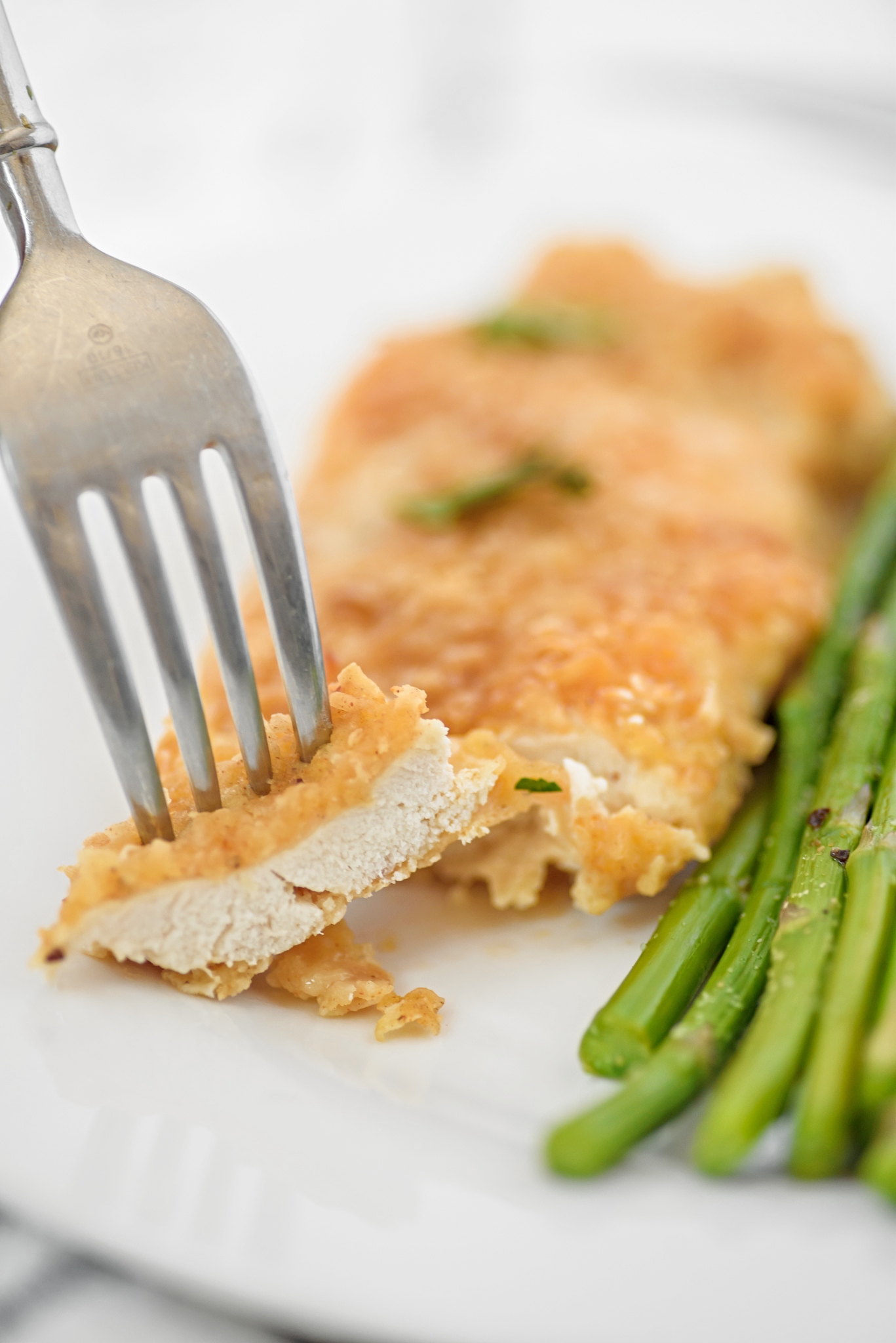 Boneless chicken with a flavorful parmesan crust, paired with asparagus on a white plate