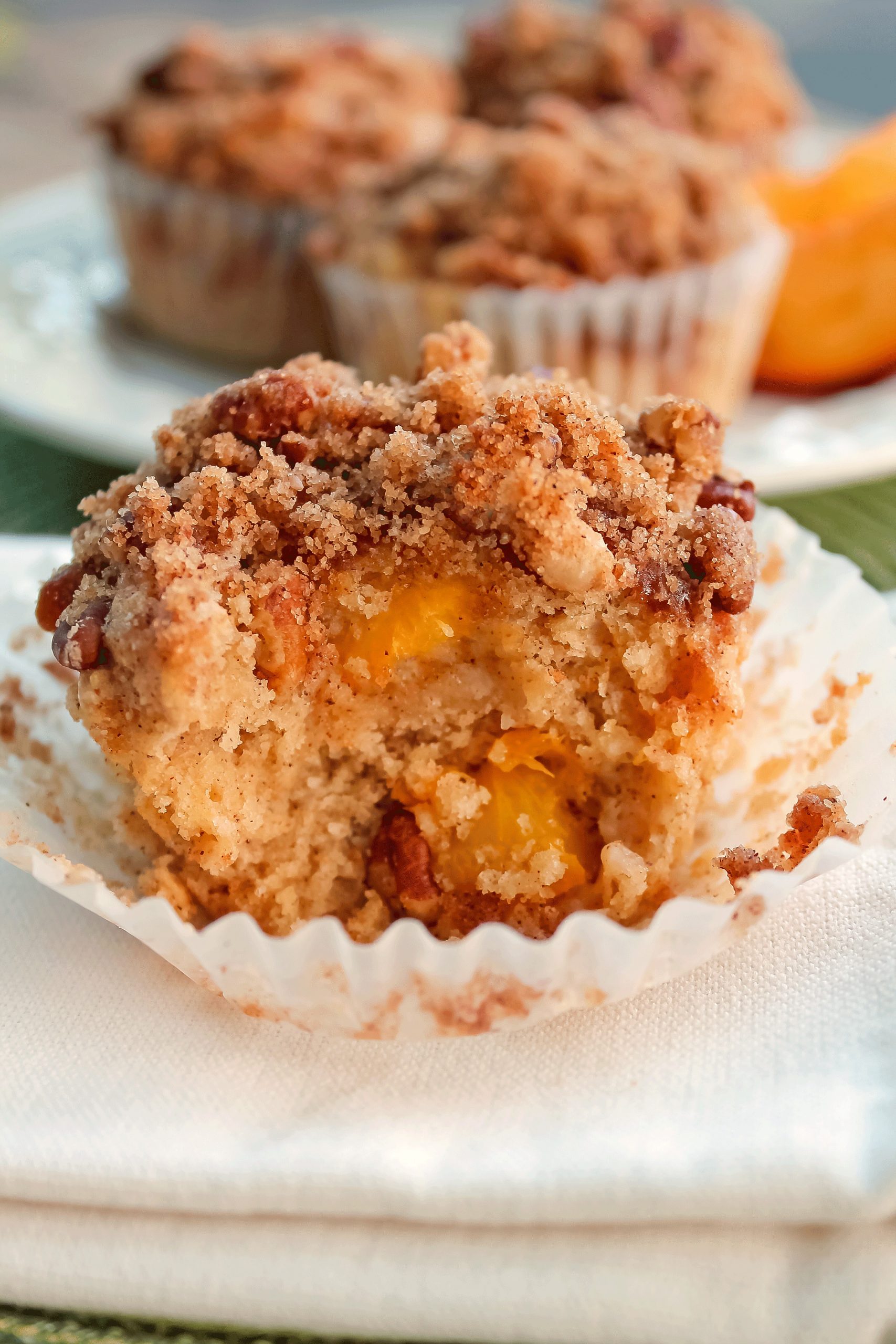 An open half muffin filled with cubed peaches, topped with crumb topping 