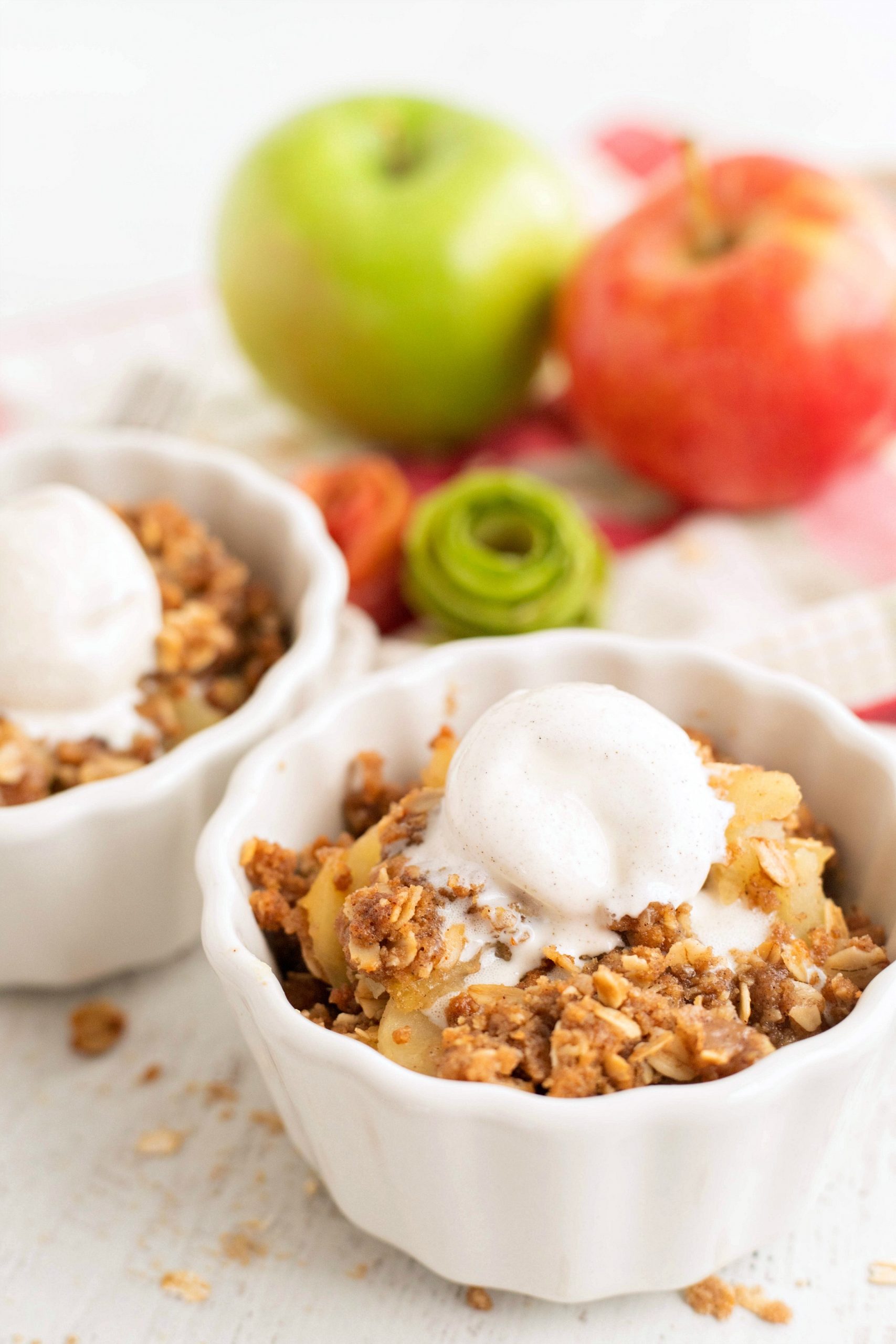 Two desserts cups with apple crisp topped with a scoop of ice cream.
