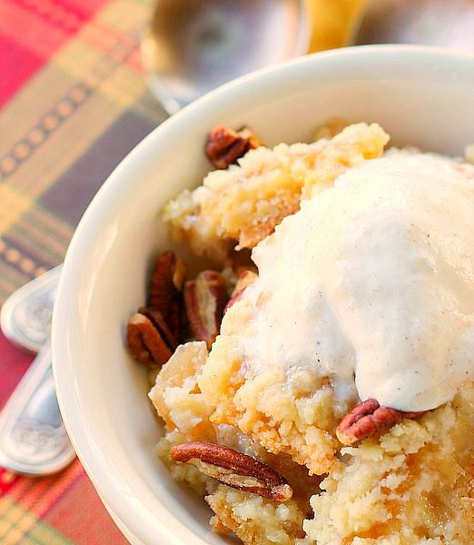 A white bowl of sugar cookie apple crisp with pecans and topped with ice cream