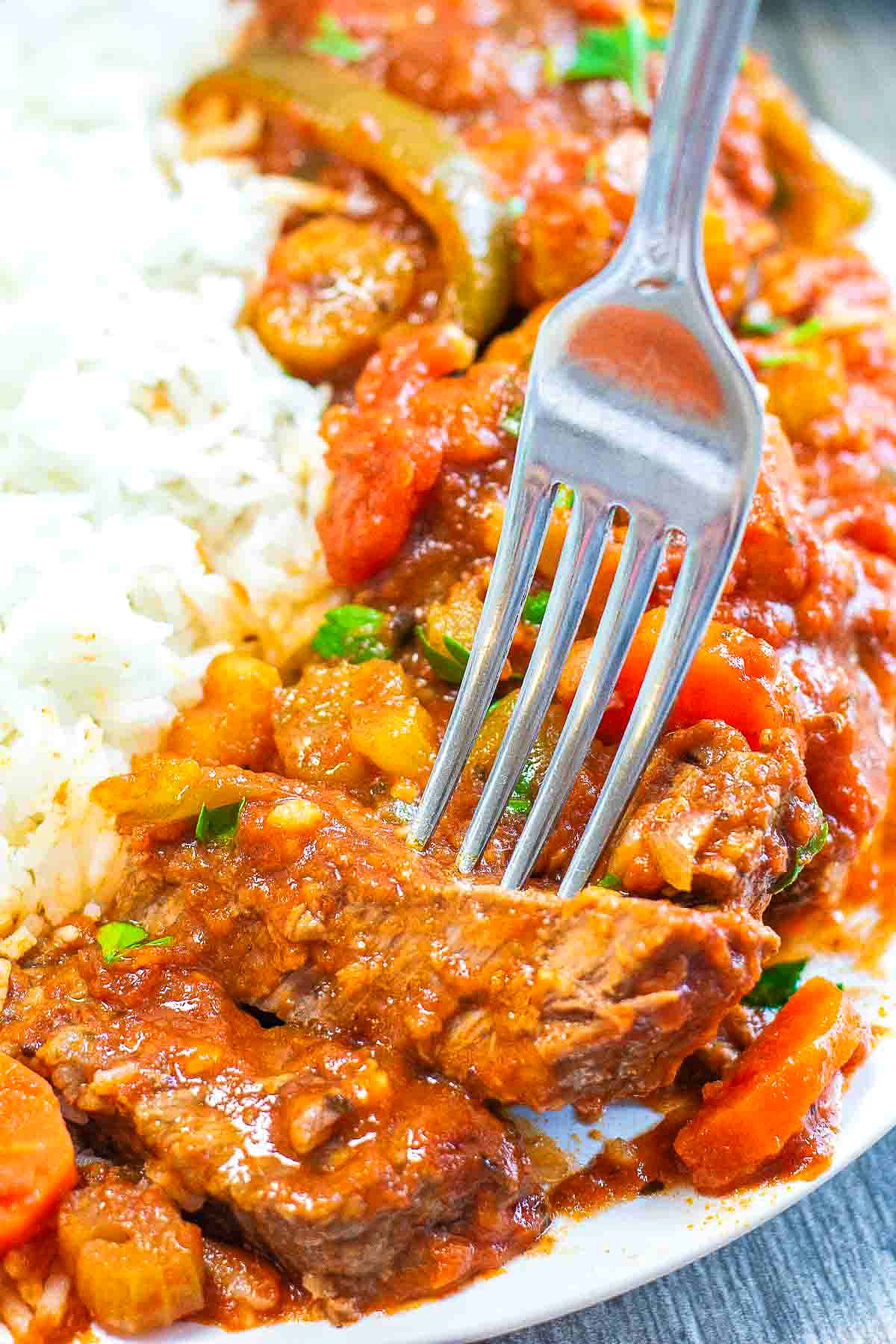 Tender steak covered in tomato sauce with vegetables over a bed of rice.