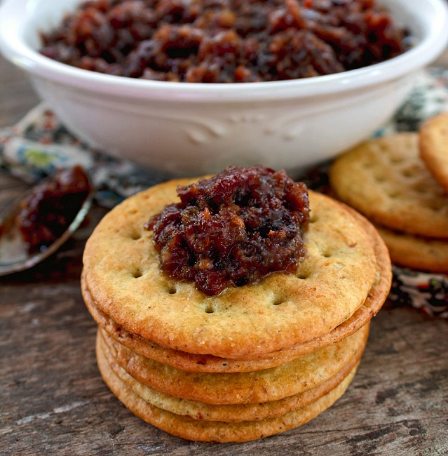 Bacon jam in a white bowl as well as on a cracker on a wooden table