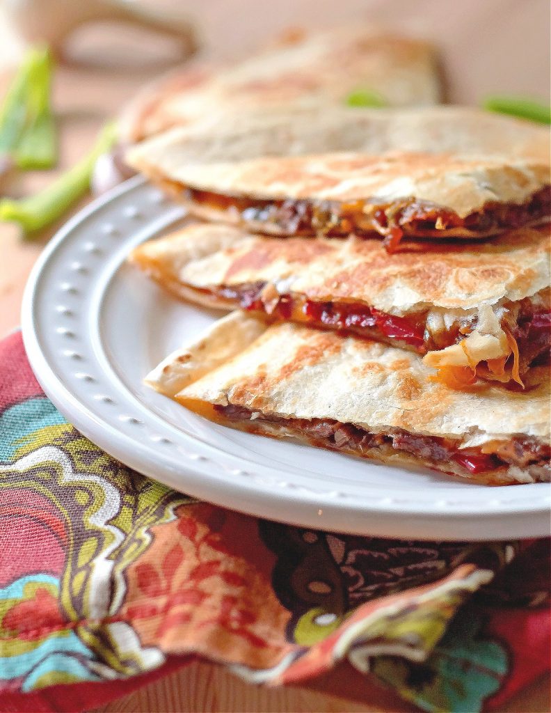 Three delicious quesadillas with steak, peppers, onions, and melted cheese on a white plate
