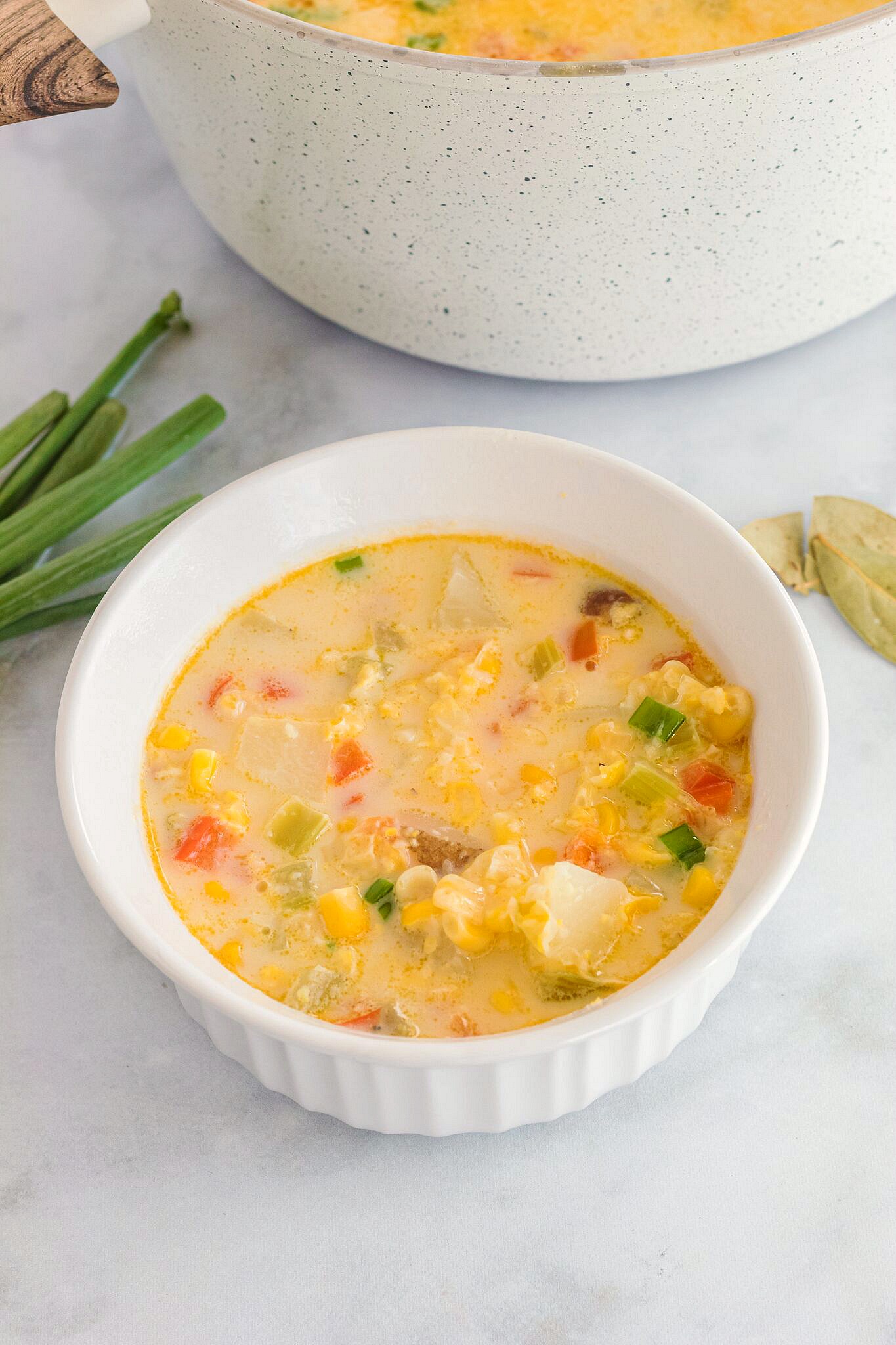 White bowl with vegetables and creamy corn chowder on a white table