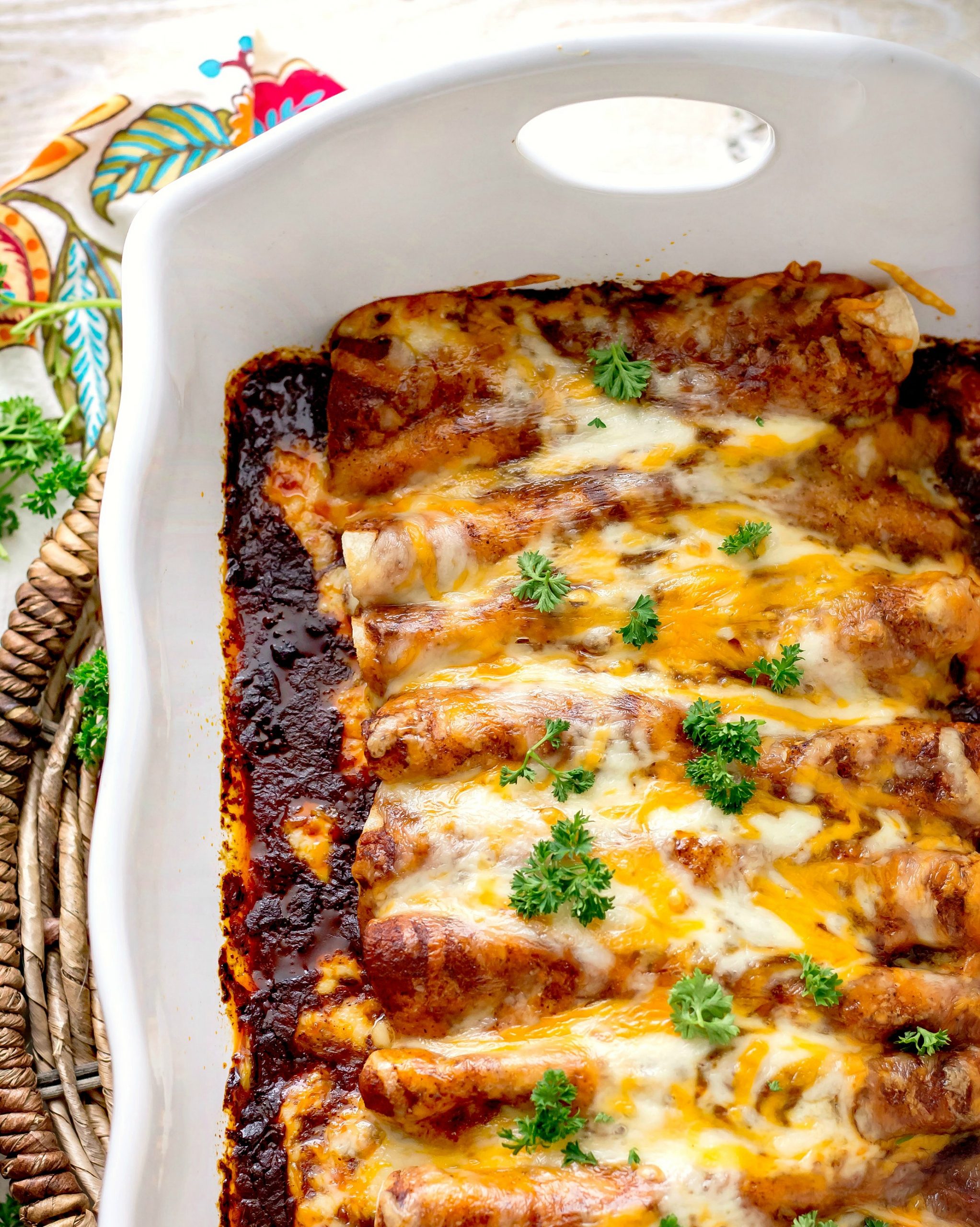 Baked Chicken Enchiladas with Homemade Red Sauce and melted cheese on top in a white baking dish