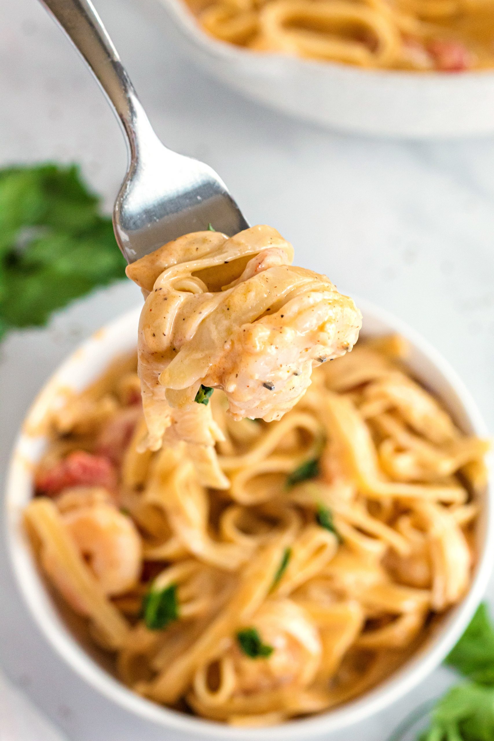 A fork full of creamy fettuccini and a bowl of fettuccini with shrimp and red peppers 