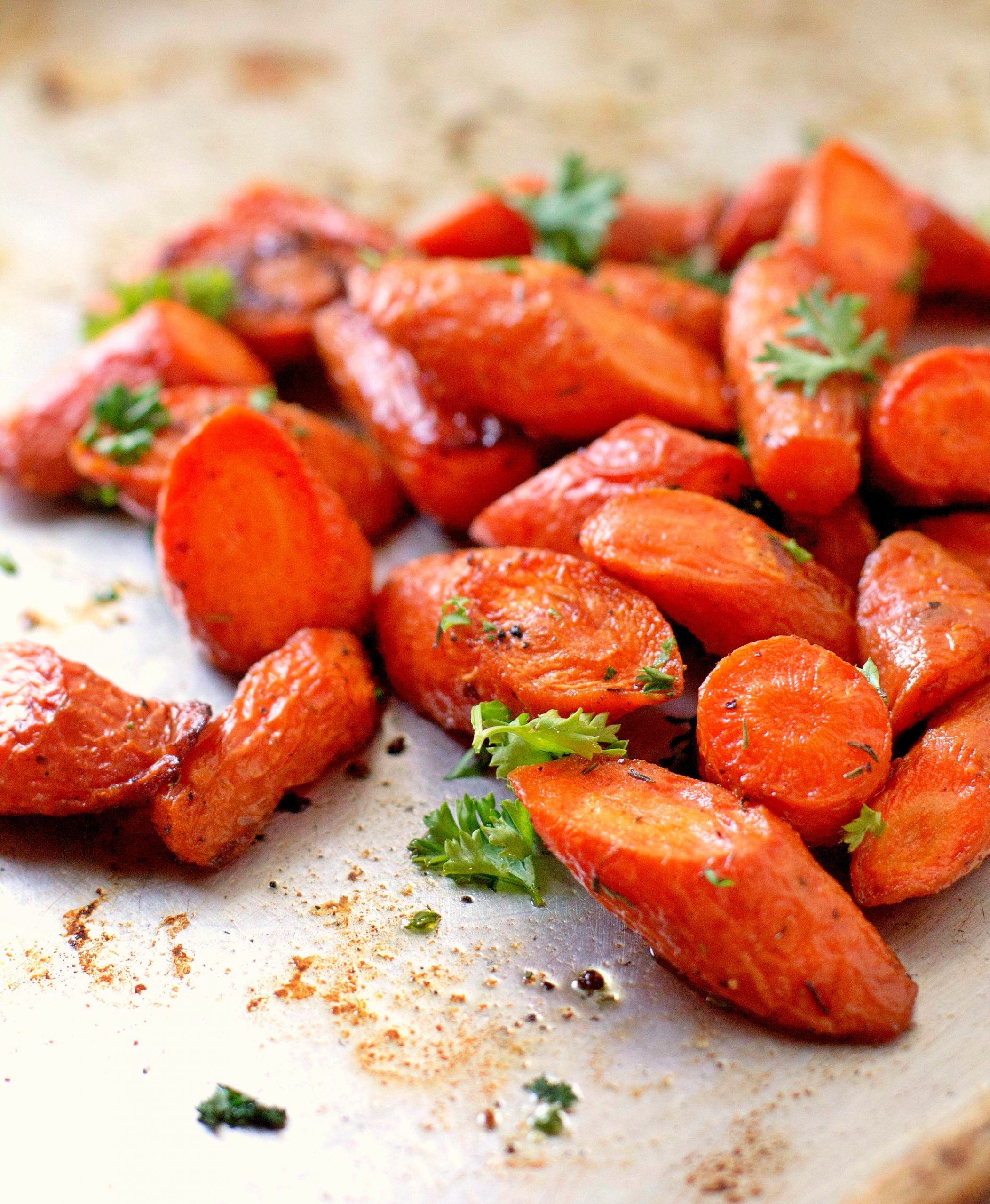 An oven sheet with roasted carrots, topped with spices and parsley
