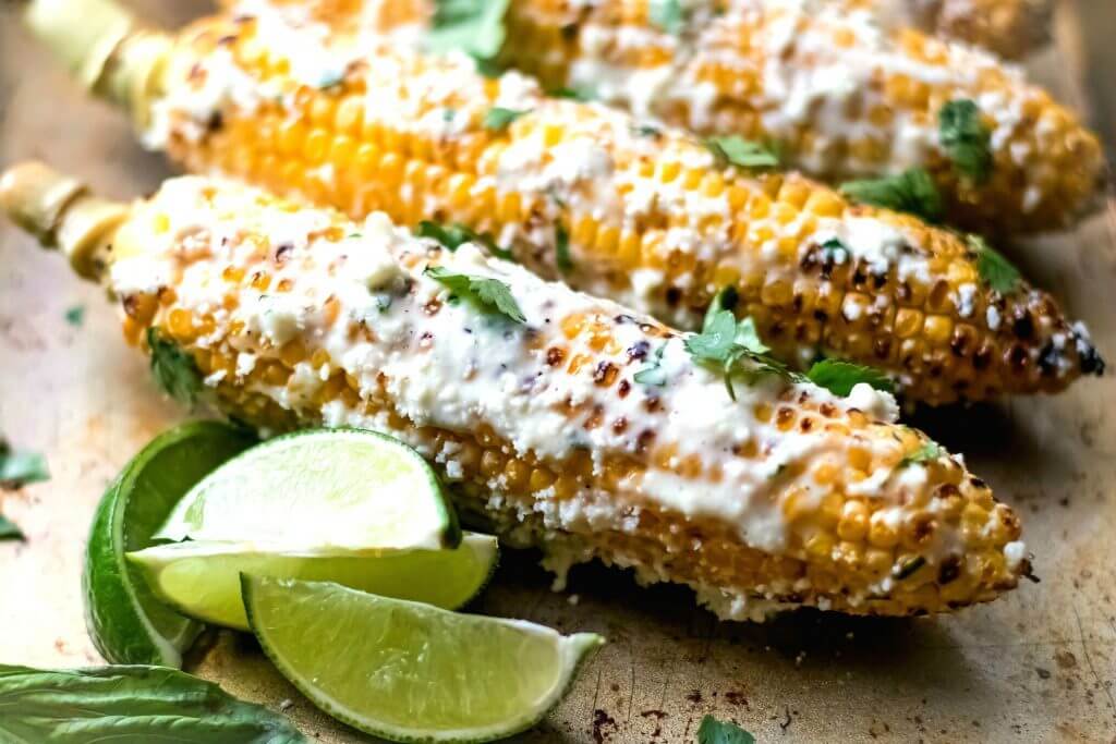 Mexican Street Corn sitting on a baking sheet garnished with cilantro and lime slices