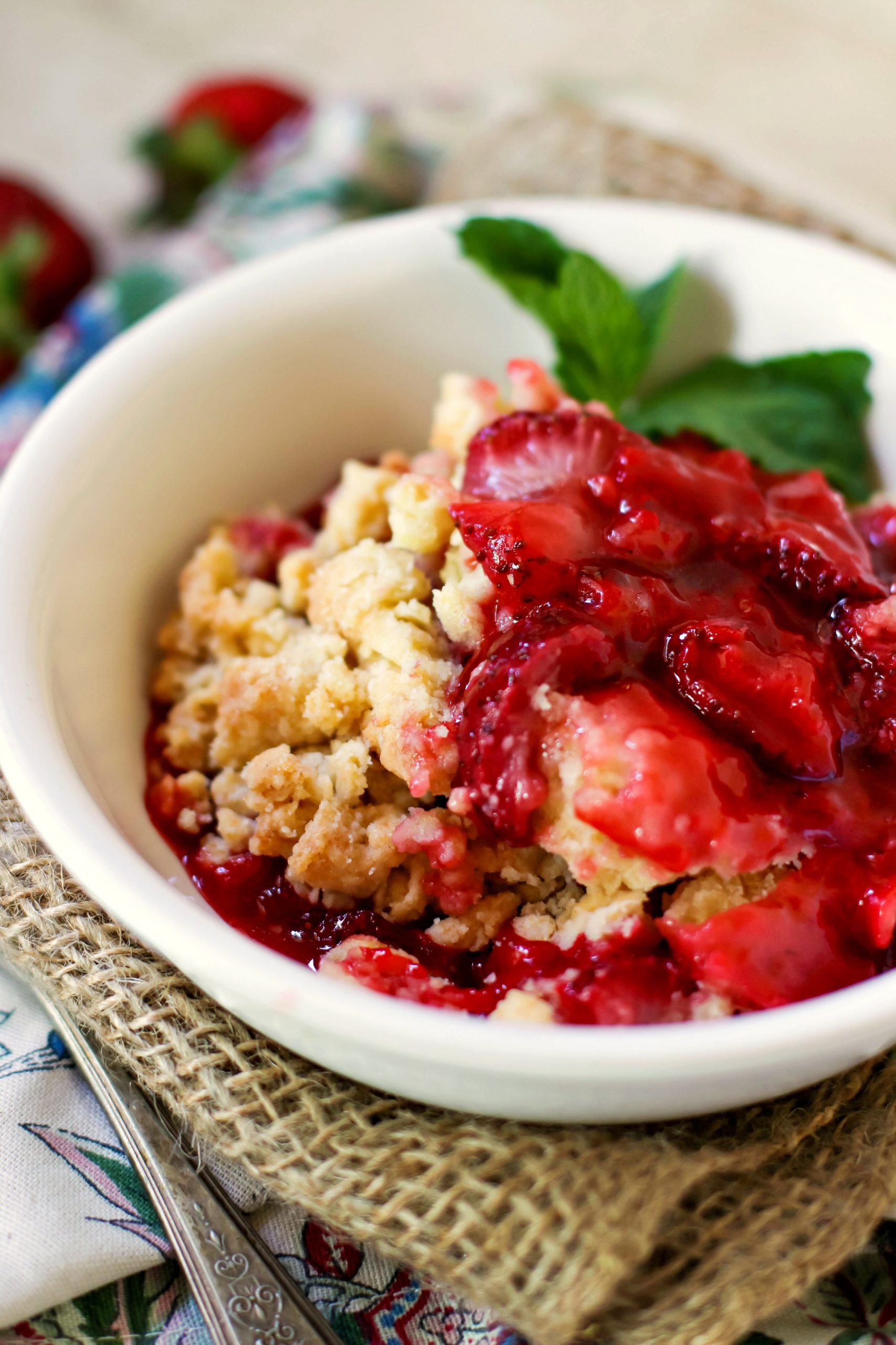 A bowl of strawberry cobbler  garnished with mint in a white bowl on a burlap napkin