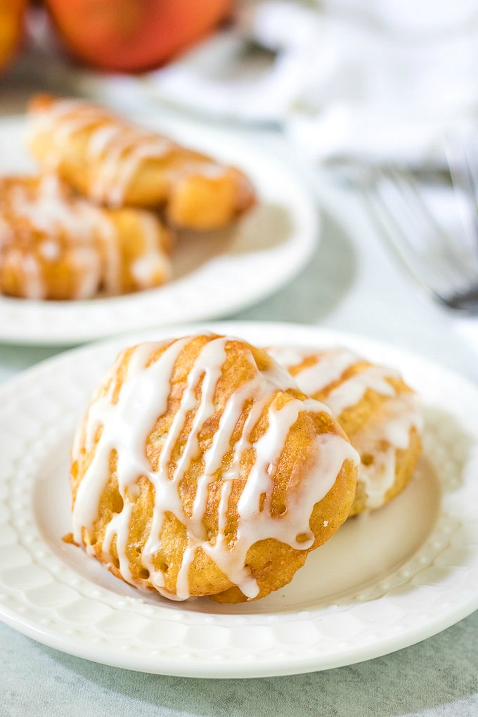 Delicious peach fritters on a plate drizzled with a glaze of confectioners sugar and milk