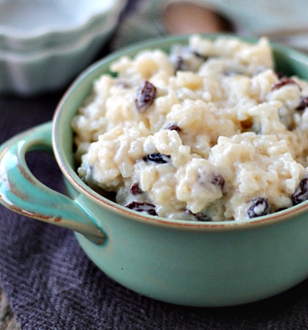 A blue dessert bowl with rice pudding in that has raisins mixed in.