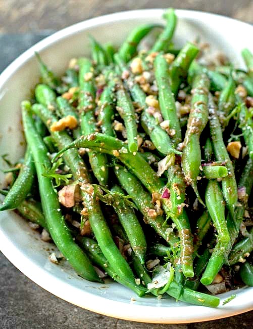 Green beans topped with chopped walnuts in a white bowl 
