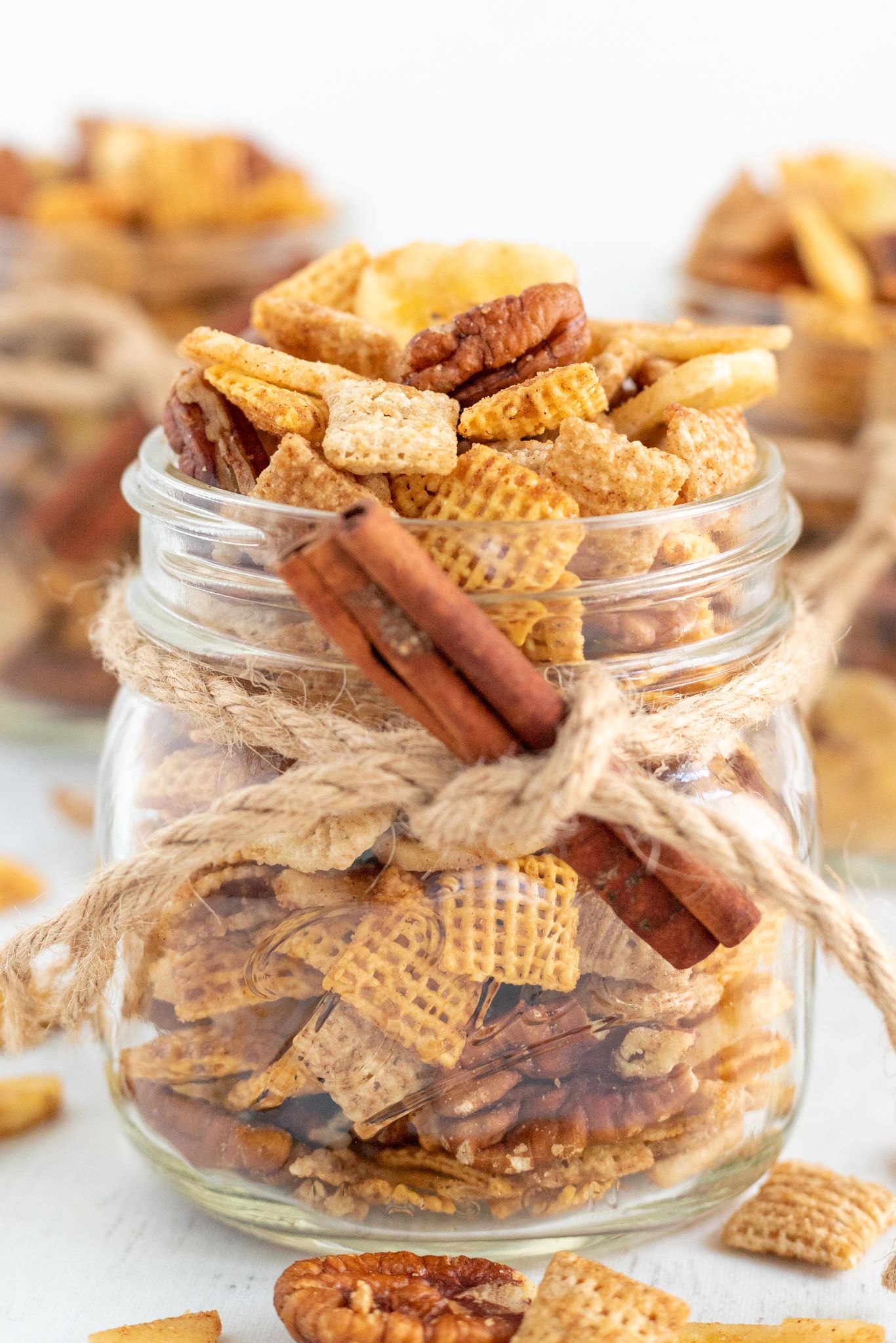 A jar of banana foster chex mix with cinnamon sticks tied onto jar