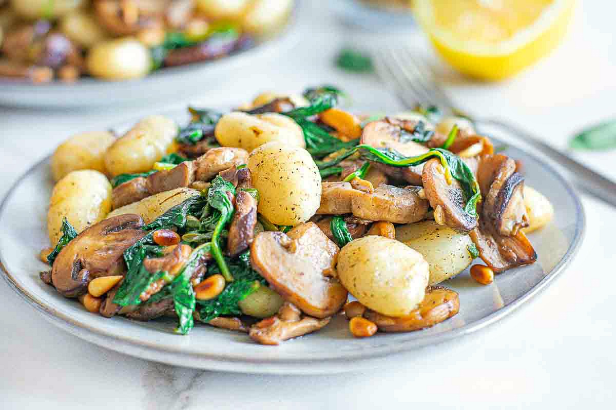 Gnocchi, mushrooms, spinach and toasted pine nuts covered in browned butter on a white plate